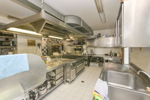 Cucina professionale dell'Hotel Le Clou ad Arvier con attrezzature in acciaio inossidabile, banchi di preparazione e cucina commerciale