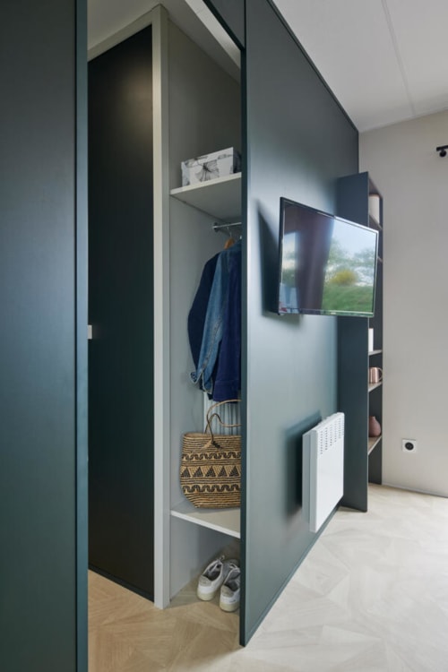 Modern hotel closet at Le Maquis Plage with dark green storage, hanging clothes, shelving, and wall-mounted TV