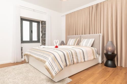 Quarto moderno em BHF Residences Arco da Calheta com cama listrada, cortinas bege e piso em madeira