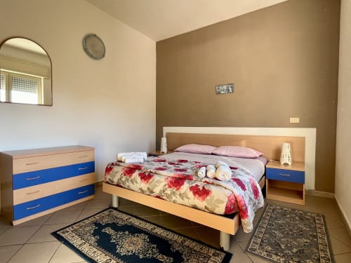 Camera luminosa dell'Appartamento Tirreno a Tirrenia con letto matrimoniale, cassettone blu e legno, specchio e pavimento in piastrelle