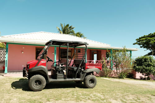 Vehículo rojo de servicio estacionado en la boutique lodge Seaflower en San Andrés, Colombia, con edificio rosa y palmeras