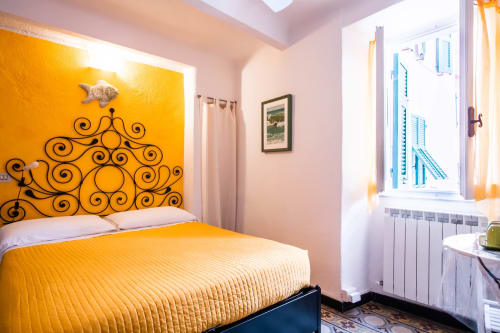 Luminoso letto giallo con testata in ferro battuto nella camera SoleMagia B&B, Vernazzo Italia, con vista della città