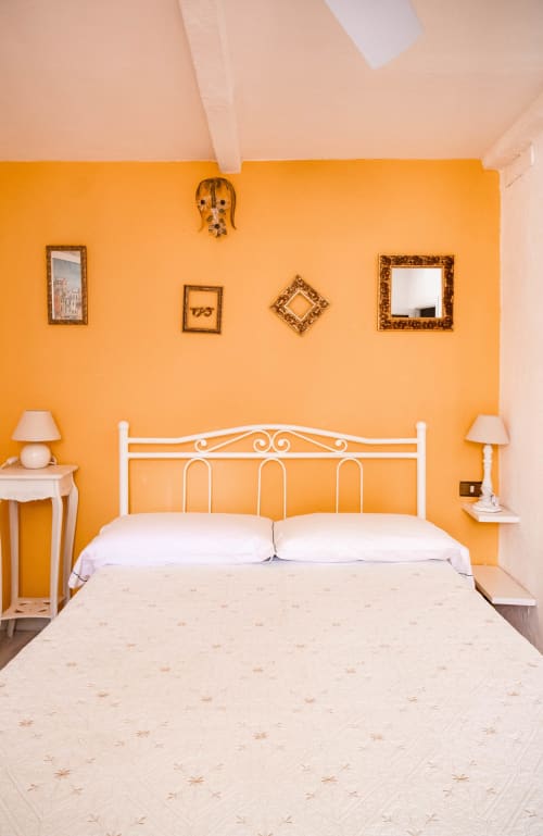 Camera luminosa arancione con letto in metallo bianco, specchi con cornici dorate e beige presso SoleMagia B&B a Vernazza, Italia