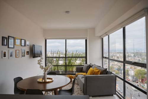 Apartamento moderno en CDMX con vistas a la ciudad, sofá gris, mesa de comedor redonda y ventanales que enmarcan la vista de la Ciudad de México