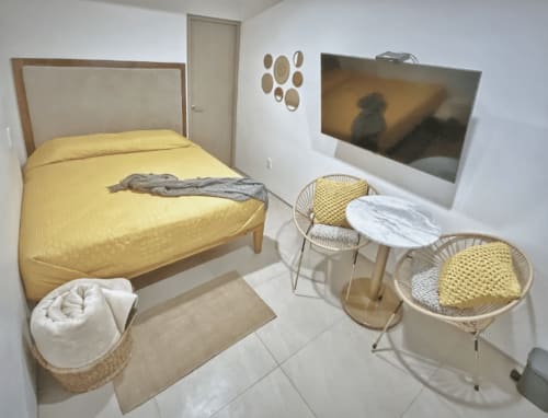 Recámara moderna en Pares Homes CDMX con cama amarilla, sillas tejidas y TV en la pared