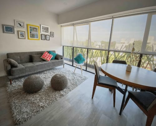 Apartamento moderno en CDMX de Pares Homes con sofá gris, mesa redonda de comedor y vistas a la ciudad desde ventanales.