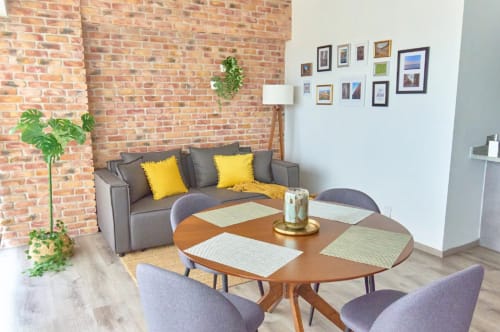 Sala de un moderno apartamento en Ciudad de México con ladrillo expuesto, mesa de comedor redonda de madera, sofá gris con cojines amarillos y cuadros enmarcados