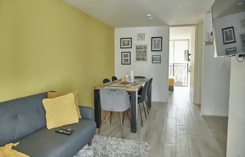Sala de estar de apartamento moderno en Ciudad de México con pared amarilla, sofá gris, mesa de comedor y cuadros en Pares Homes