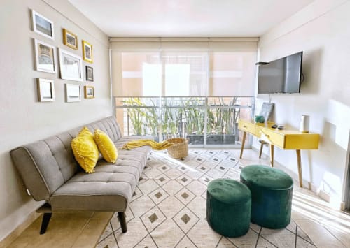 Sala moderna en CDMX con sofá gris, acentos amarillos, poufes verdes y vista al balcón en Pares Homes