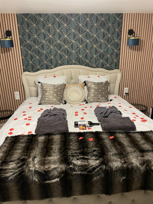 Suite de luxe avec tête de lit crème, mur d'accent à motifs, cœurs rouges romantiques et plaid en fausse fourrure à Chartrettes
