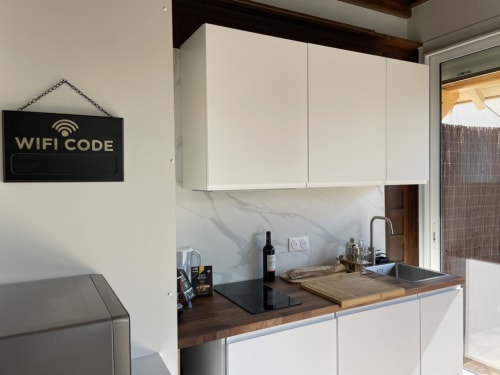 Cuisine moderne avec armoires blanches, plan de travail foncé et affichage du code WiFi dans un gîte français