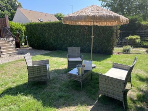 Espace de détente du jardin avec fauteuils en osier, parasol de chaume et haies à Suite d'amour et détente à Chartrettes