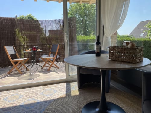 Appartement moderne avec table ronde noire, terrasse avec vue sur le jardin, transats et paravents en rotin dans ce gîte français