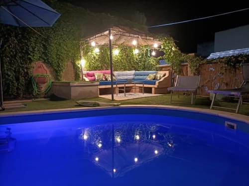 Piscina illuminata della Maison Belle Époque a Oristano con area lounge e pergolato ricoperto di edera di notte