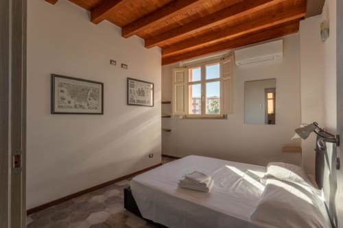 Camera luminosa presso Maison Belle Époque a Oristano con travi in legno a vista, biancheria bianca e opere d'arte incorniciate alle pareti.