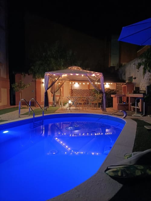 Piscina illuminata di notte con luci blu, gazebo e patio presso Maison Belle Époque a Oristano