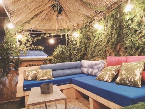 Accogliente lounge all'aperto presso Maison Belle Époque a Oristano con sedute blu, piante sospese e tetto in paglia di notte