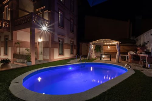 Piscina illuminata di blu presso Maison Belle Époque a Oristano, Italia, con edificio e gazebo illuminati di notte
