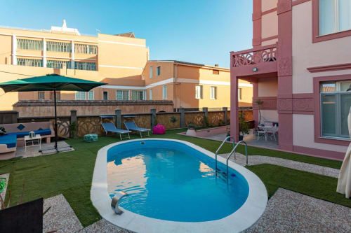 Piscina della resort con acqua blu, lettini prendisole e edifici colorati presso Maison Belle Époque a Oristano