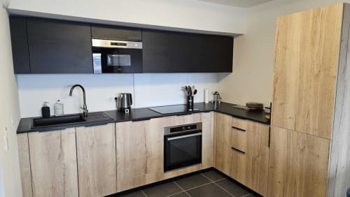 Cuisine moderne dans l'appartement d'Aime-la-Plagne avec meubles en bois, plan de travail noir et électroménagers intégrés