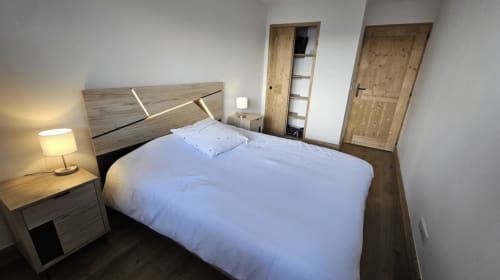 Chambre moderne de l'hôtel L'écrin des sapins à Aime-la-Plagne avec lit en bois, draps blancs et portes en bois