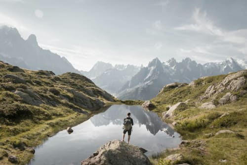 Randonneur admirant un lac alpin avec des montagnes enneigées, L'écrin des sapins, Aime-la-Plagne