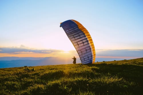 Parapentiste décollant d'une prairie de montagne au coucher du soleil près de L'écrin des sapins à Aime-la-Plagne, Savoie