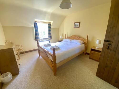Bright bedroom with wooden double bed, blue pillows, yellow walls, and window at Leitrim Quay cottage in Ireland