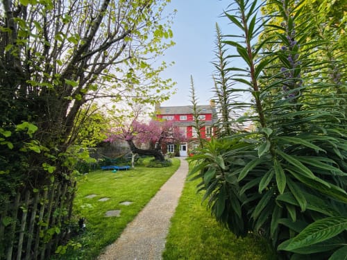 Allée du jardin de L'Ermitage B&B à Saint-Vaast-la-Hougue avec verdure luxuriante et bâtiment en brique rouge