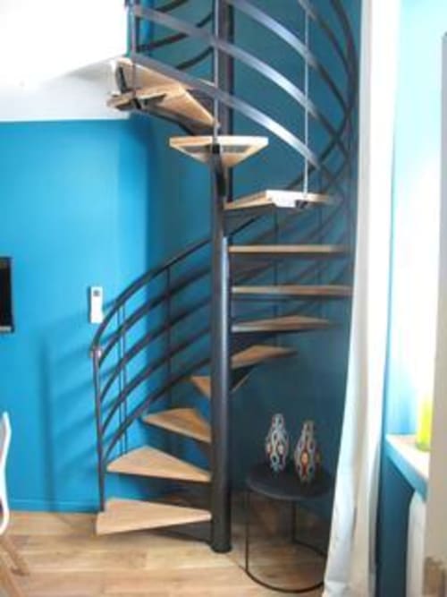 Spiral staircase with wooden steps and metal railing in bright blue modern apartment at AJOUCADOU, Lourmarin