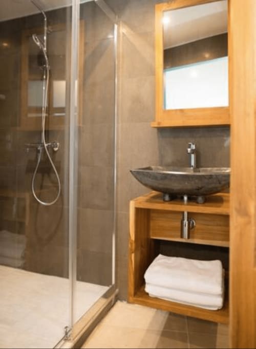 Modern bathroom in The Nest apartment at AJOUCADOU BnB in Lourmarin with stone vessel sink, wooden vanity, and glass shower