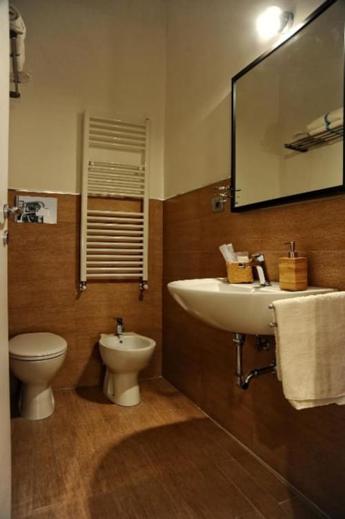 Modern bathroom in Casa Castagna's Economy Double Room, Salerno, with brown tile walls, white sink, toilet, bidet, and heated