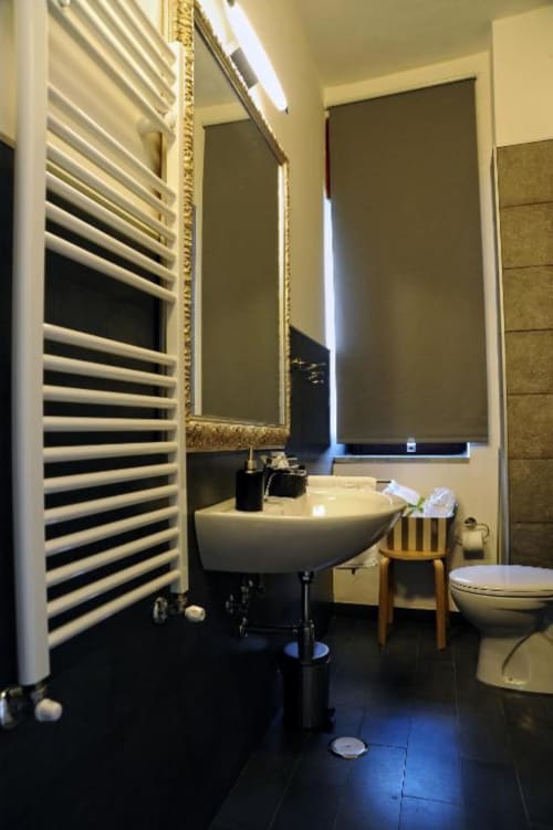 Modern bathroom at Casa Castagna Salerno with white pedestal sink, heated towel rack, mirror with gold frame, and dark tile