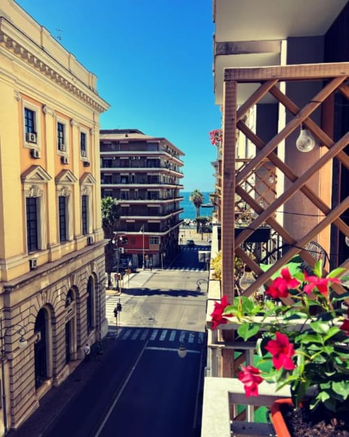 Balcony view from Casa Castagna in Salerno showing sea, city streets, and red flowers overlooking the coast