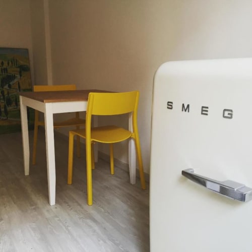 Modern kitchen with white SMEG refrigerator, small dining table with yellow chairs in Casa Castagna apartment, Salerno