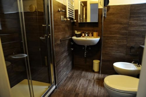 Modern bathroom at Casa Castagna Salerno with dark wood tiles, white sink, bathtub, shower enclosure, and warm lighting