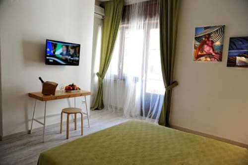 Deluxe studio apartment at Casa Castagna in Salerno with green bedding, desk, TV, and courtyard view through curtained