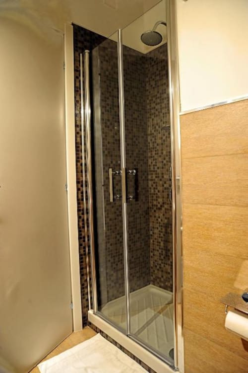 Modern shower enclosure with dark mosaic tiles and rainfall showerhead in Casa Castagna economy room, Salerno