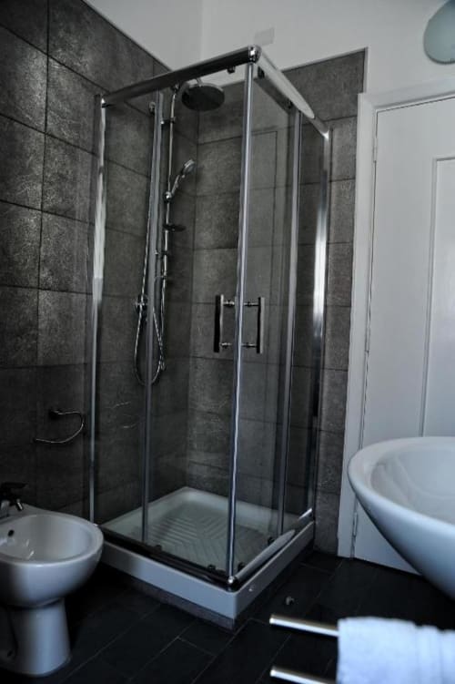 Modern bathroom with glass shower enclosure, dark tile walls, white toilet and bathtub in Casa Castagna apartment, Salerno