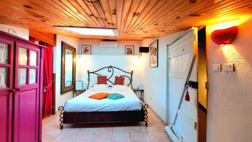 Chambre mansardée colorée à La Bergerie Du Moulin avec lit en fer forgé, portes roses et plafond en bois chaleureux