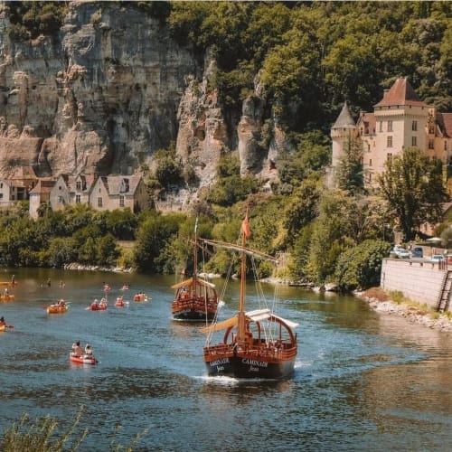 Château médiéval et village riverside en Dordogne avec barques traditionnelles et habitations troglodytes
