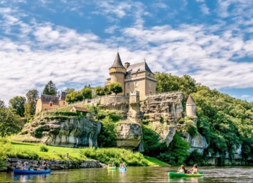 Château médiéval perché sur une falaise rocheuse dominant la rivière avec bateaux, entouré d'un paysage verdoyant près de Thénon, France
