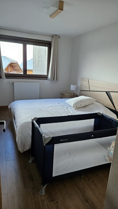 Chambre moderne de l'hôtel L'écrin des sapins à Aime-la-Plagne avec lit double, lit parapluie, vue fenêtre et parquet.