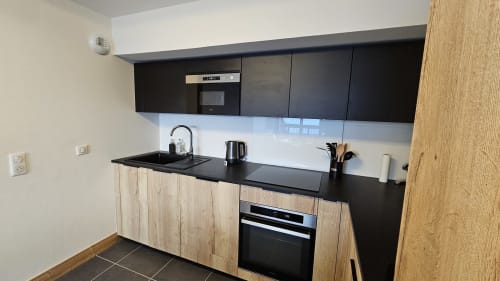 Cuisine moderne avec plan de travail noir, placards en bois et électroménagers intégrés à L'écrin des sapins à Aime-la-Plagne