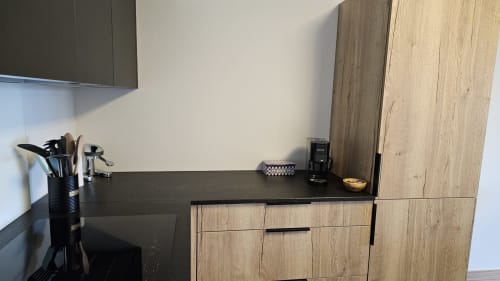 Comptoir de cuisine moderne avec plan de travail noir, armoires en bois, porte-ustensiles et électroménagers à L'écrin des sapins,