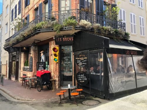 Les Docks café with black storefront and planters at Hotel Le Trouville in Trouville sur Mer