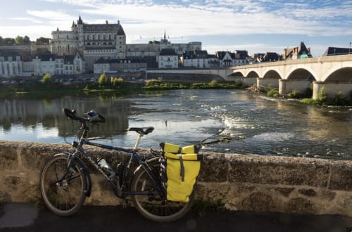 Vélo avec sacoche jaune au bord de la Loire, château de Blois et pont de pierre en arrière-plan