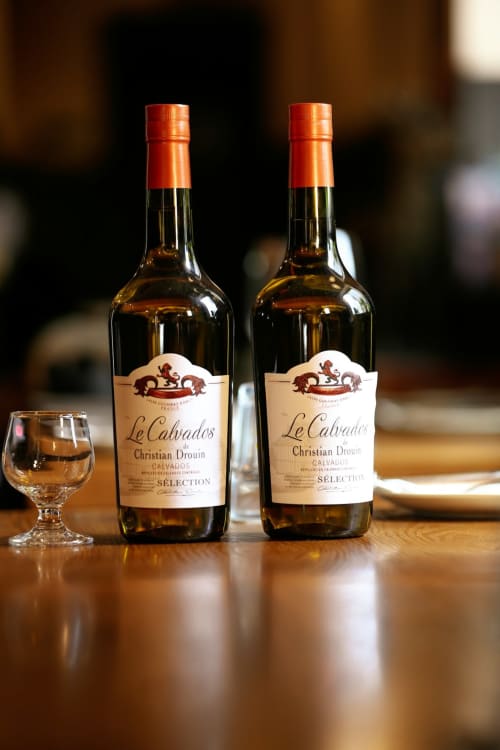 Deux bouteilles de Calvados Christian Drouin Selection exposées sur table en bois à l'Hôtel Le Trouville en Normandie,
