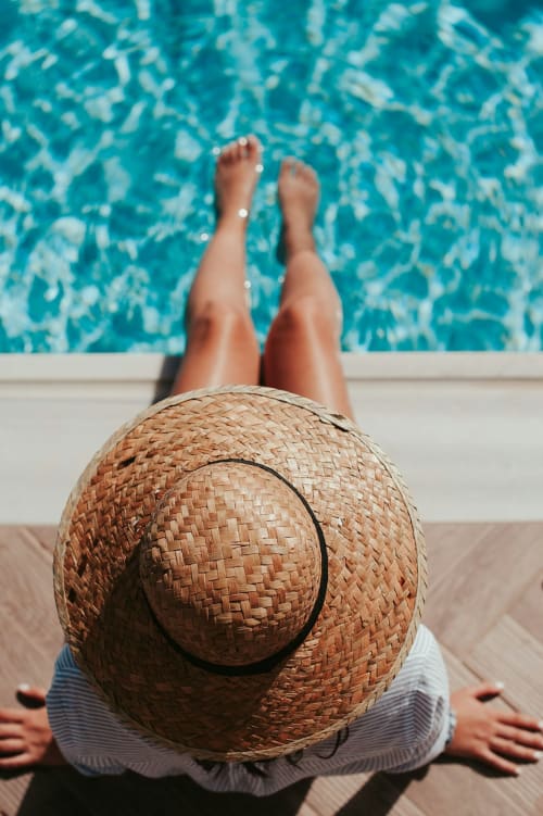 Personne détente au bord de la piscine de l'Hôtel Le Trouville, Trouville-sur-Mer, coiffée d'un chapeau de paille, pieds surélevés