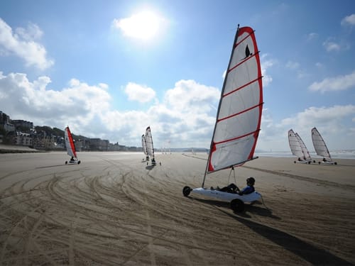 Bateaux à voile de sable aux voiles rouges sur la plage de Trouville sous un ciel bleu avec des bâtiments côtiers
